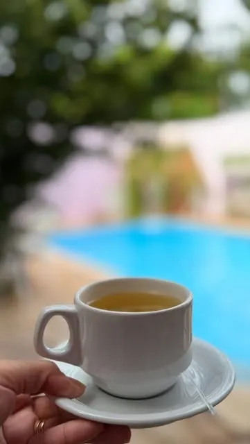 Xícara de chá na mão, com a piscina e o jardim desfocados ao fundo.