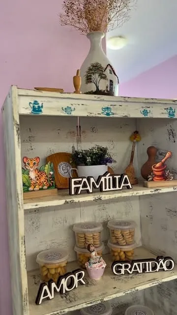 Estante de madeira pintada com bules desenhados, potes de biscoito e as palavras Família, Amor e Gratidão.